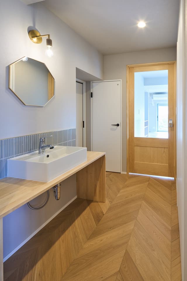 来客時にとっても便利な、廊下の造作洗面。ブランケット照明、鏡、タイルの淵に真鍮のアクセントが入っています。両サイドのテーブルは、手洗い時に荷物を置いたり、掃除のときにも重宝します。