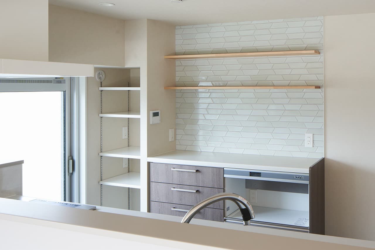 キッチンの壁は不揃いのタイルを貼り合わせています。キッチン奥のパントリーは、ストック食材などを入れるのに便利です。リビングから2つ目のベランダに出ることもできます。日中も明るく、窓を開ければ換気もバツグンです。