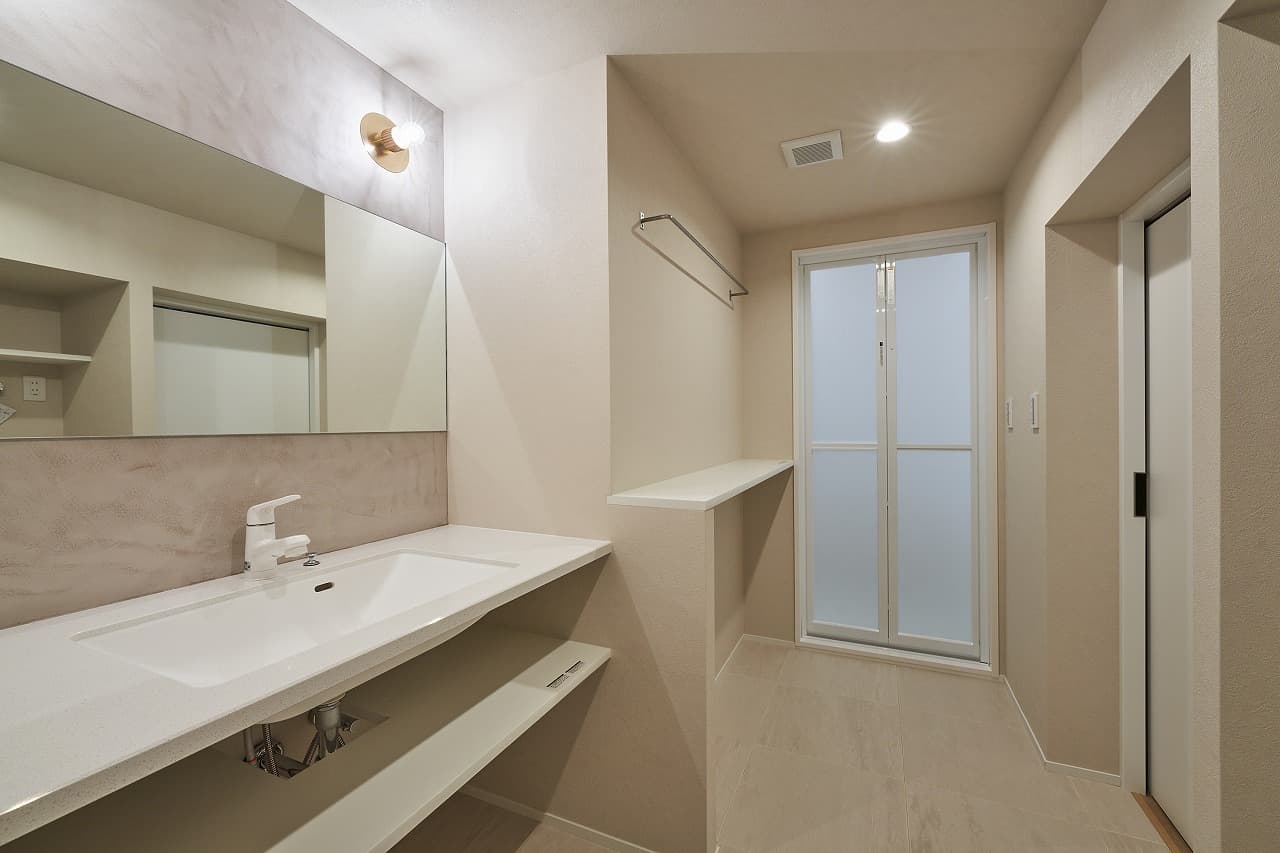 水回りスペースです。造作洗面は、小豆色がめずらしいモルタル塗装に、めずらしい形のブランケット照明を左右に2つつけました。忙しい朝、家族が並んでもゆったりと過ごすことができます。洗面後ろには洗濯機が置けるスペースがあります。