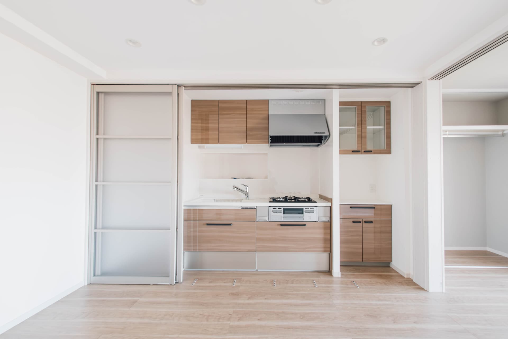 キッチン。サイズはミニマルで、右の棚を含め収納が充実しています。食洗機はついていません。来客があるときに水回りを隠せる引き戸がついています。