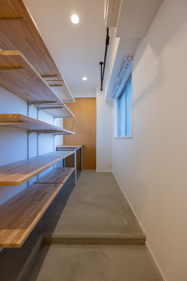 玄関入って右手の、シューズクローゼット兼ワークスペース。奥にワークスペースを設けることで、秘密基地のような雰囲気に仕上がりました。
ハンガーバーをつけており、コートなどをかけておくことができます。
シューズクローゼットは可動式の棚のため、下にはスーツケースも収納可能です。