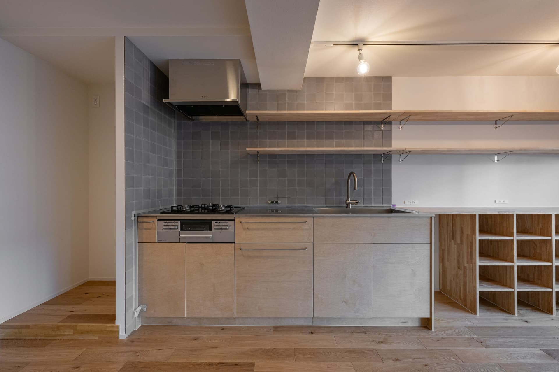 キッチン。3口コンロで広々としたキッチンで、収納もたくさんあるので困りません。棚もつけているため、コーヒーカップなどを飾っています。
左側に冷蔵庫を置いていますが、仕切りの壁があるため、油はねなどは気にならずに使えます。
タイルの色味がアクセントです。