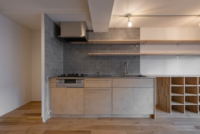 キッチン。3口コンロで広々としたキッチンで、収納もたくさんあるので困りません。棚もつけているため、コーヒーカップなどを飾っています。
左側に冷蔵庫を置いていますが、仕切りの壁があるため、油はねなどは気にならずに使えます。
タイルの色味がアクセントです。