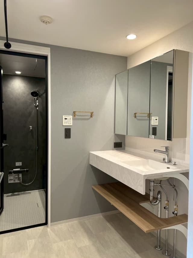 洗面所。
アイカ製の洗面台です。洗面台の上、中段、床側にそれぞれコンセントを付けました。
洗面台の並びに洗濯機スペースあり。
左側には大容量の備え付けの棚があり、日用品やタオルを収納しています。