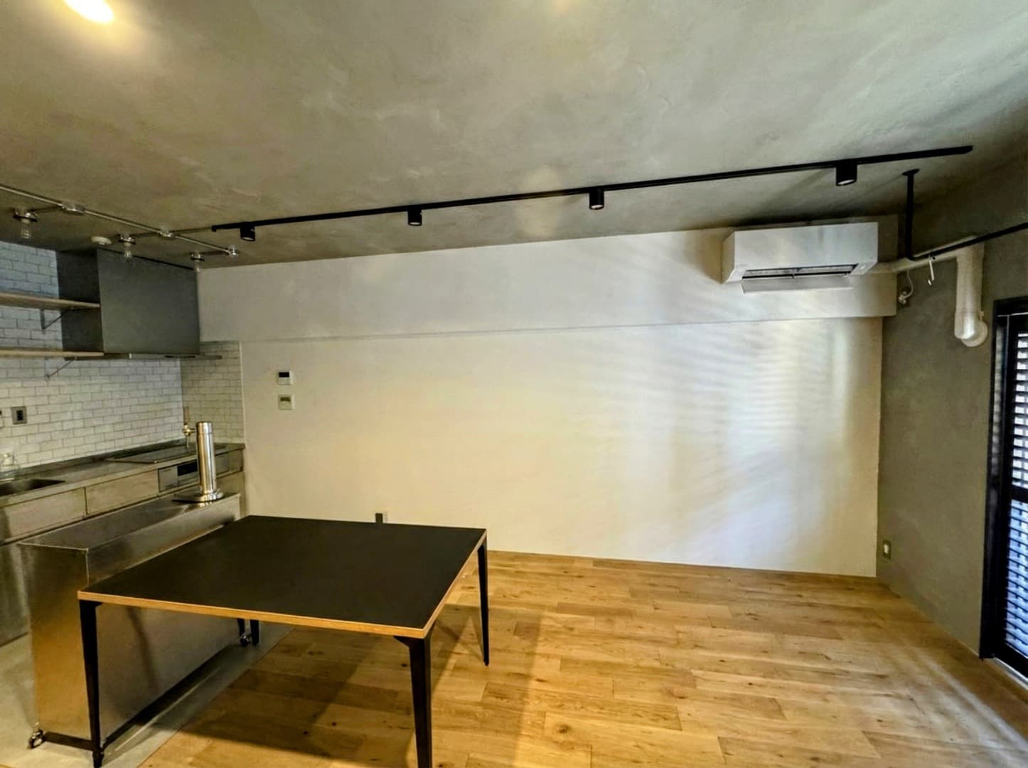 LDK②：miratap製のオースステンレスキッチン(食洗機付き)が壁付で設置してます。天井と壁はモルタル塗り壁です。インダストリアルな雰囲気を出すためにソケット電球や配管を見せる装飾にしています。