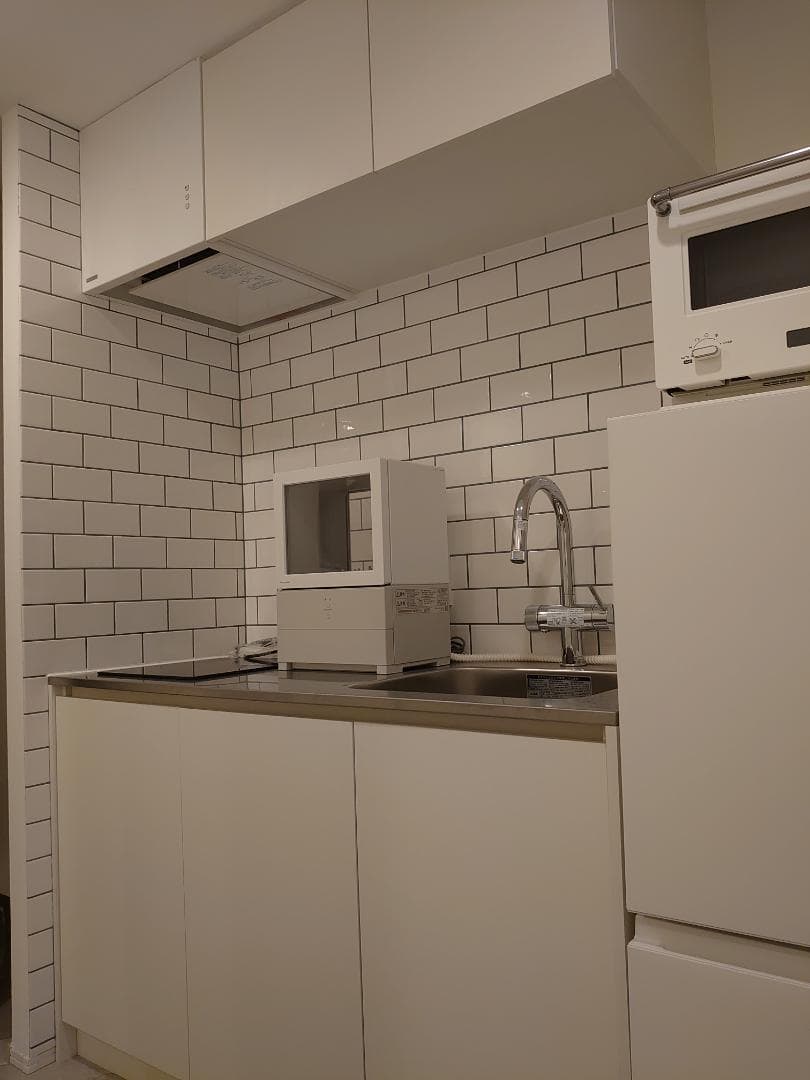 ホワイトで統一をした唯一無二なミニマムコンパクトなキッチンエリアです。
平田タイルの白いサブウェイタイルに目地は上品なセラドンカラー＊キッチンの天板はステンレスのバイブレーション仕上げ＊三化工業のモダンなIH＊水栓は浄水器機能付きハイグレード仕様のグローエ社のミンタ。もし売却をするときには未使用のPanasonic食洗機もお付けさせていただきます。※冷蔵庫と電子レンジは付きません。