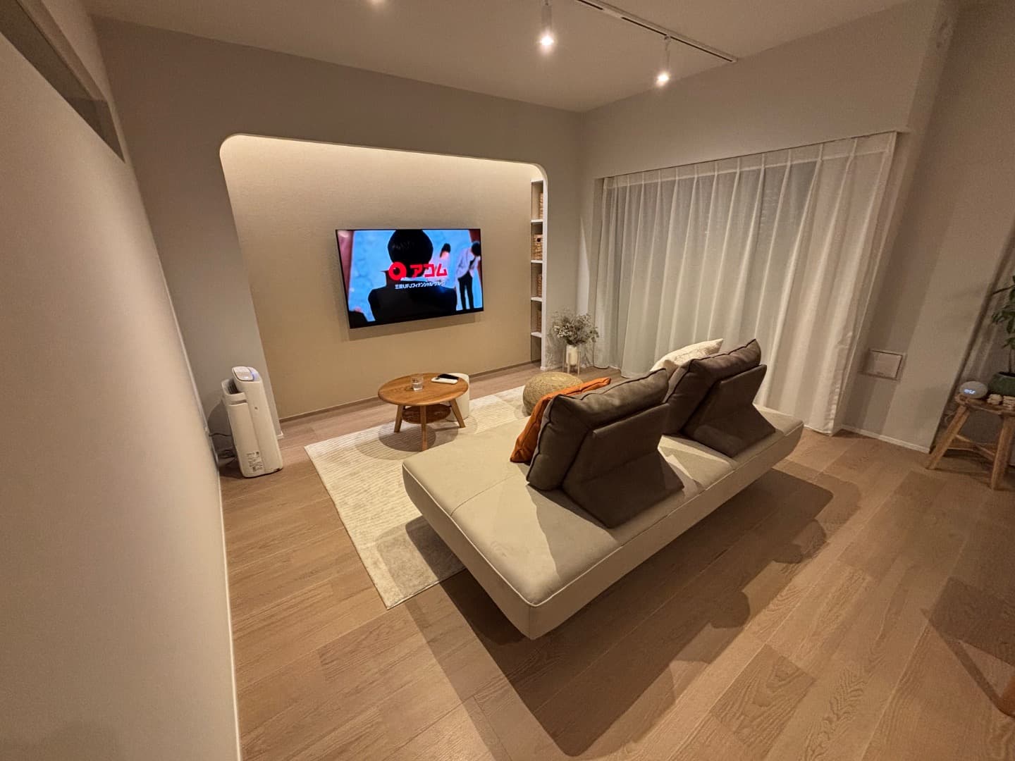 LDK入口からリビングを見る。テレビ設置面にはアーチ壁、アクセントクロス、間接照明を配置。アーチ壁の両脇には可動棚を設置し、リビングの小物を収納可能。