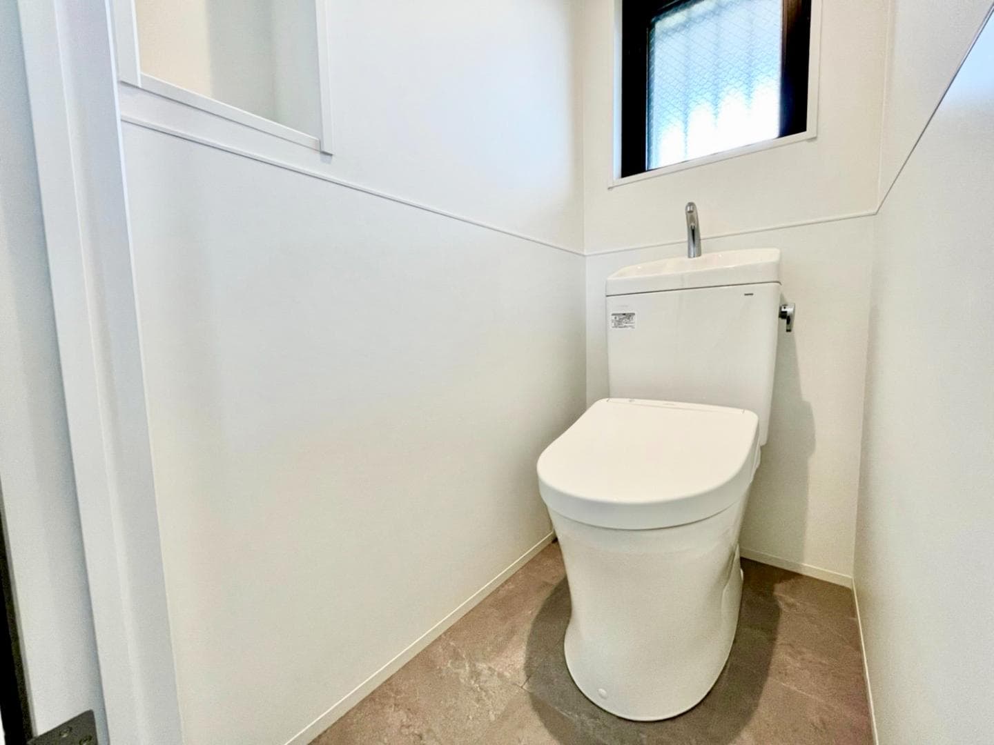 トイレはTOTO製のウォシュレット機能付き。床はグレーの水まわりに強いフロアタイル、壁は塗り壁に馴染むよう腰高から下はマットホワイトのキッチンパネルを施工。清掃性と美しさを両立させました。